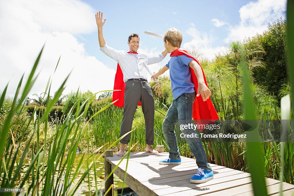 Father and son (6-7) fighting with wooden swords on pier