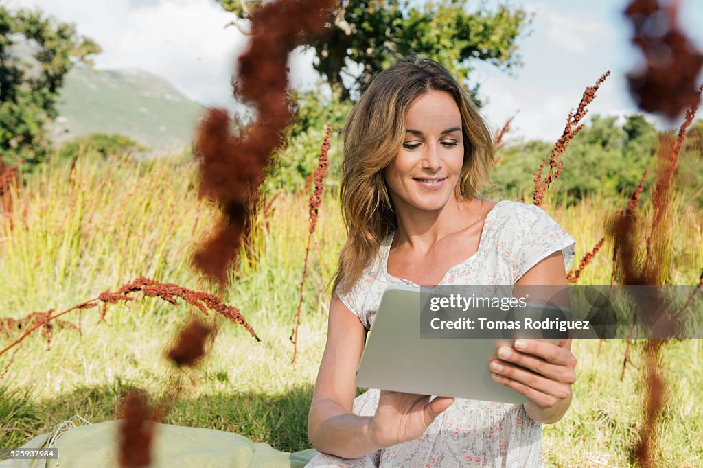 Young woman sitting among grass and using digital tablet