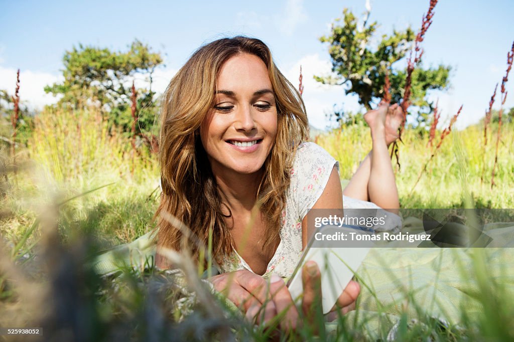 Young woman sitting among grass and using smartphone