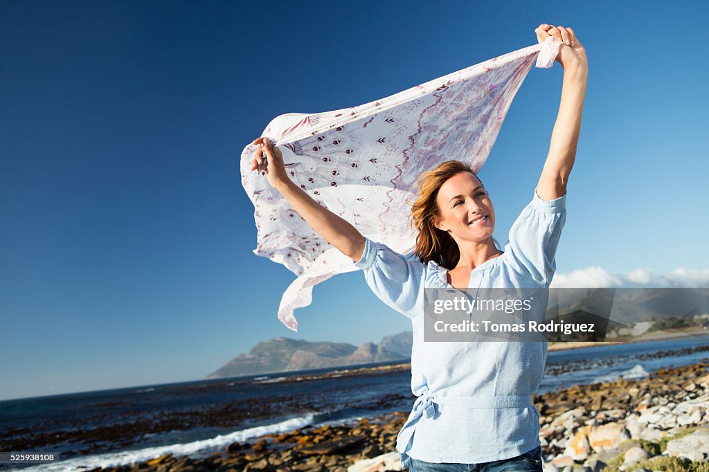 Young woman standing on sea shore with scarf blown by wind