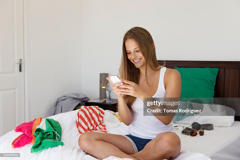 Young woman sitting on bed and texting on phone