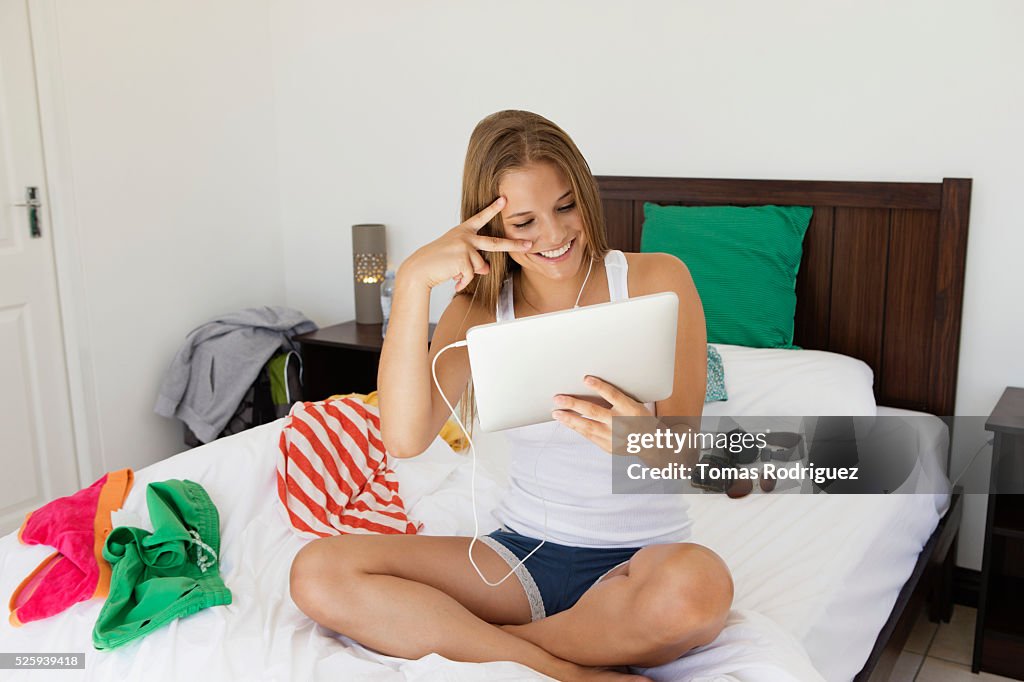 Young woman sitting on bed making faces to tablet pc