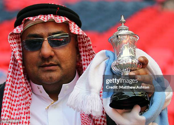 Manchester City fan dressed as a sheik holds up a replica FA Cup Trophy