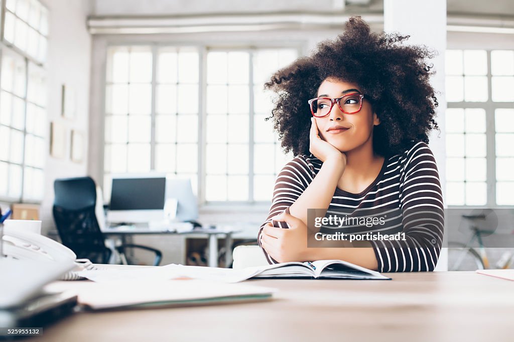 Pensive young businesswoman sitting on desk