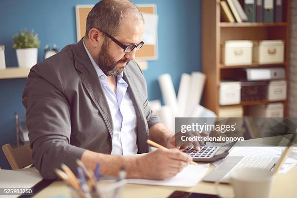 mature adult man working in the office - calculator tax forms stockfoto's en -beelden