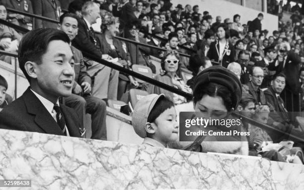 Crown Prince Akihito of Japan watches the start of the marathon at the 1964 Tokyo Olympics, accompanied by his wife Michiko and their son Naruhito .