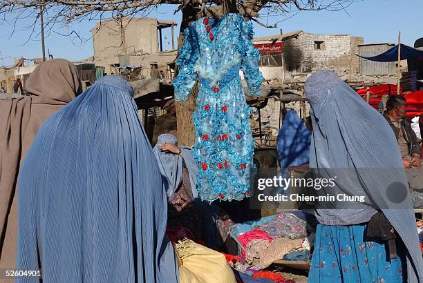 Covered women in burkas look at a western style dress for sale at a market on January 28, 2002 in Kabul, Afghanistan. Despite the fall of the...