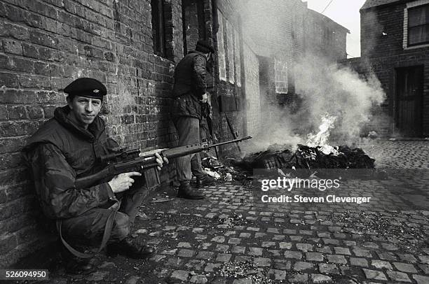 British soldier provides cover for his fellow soldiers while they check out a burning building. The IRA was known to set fire to a building and wait...