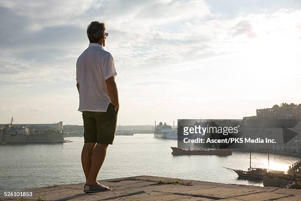 man looks out across harbour and old city, sunrise - white shorts stock-fotos und bilder