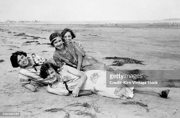 Four young women lay on the beach, ca. 1920