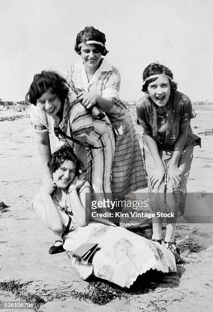 Four young women frolic and laugh on a beach, ca. 1920