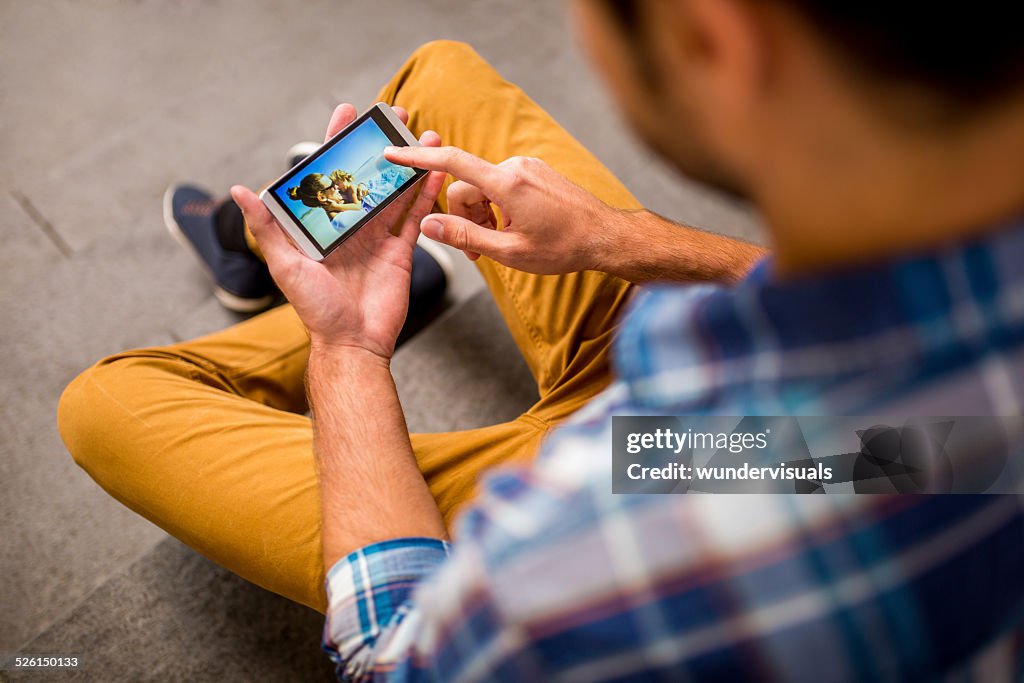 Man Looks At Photos Of Family On Smartphone