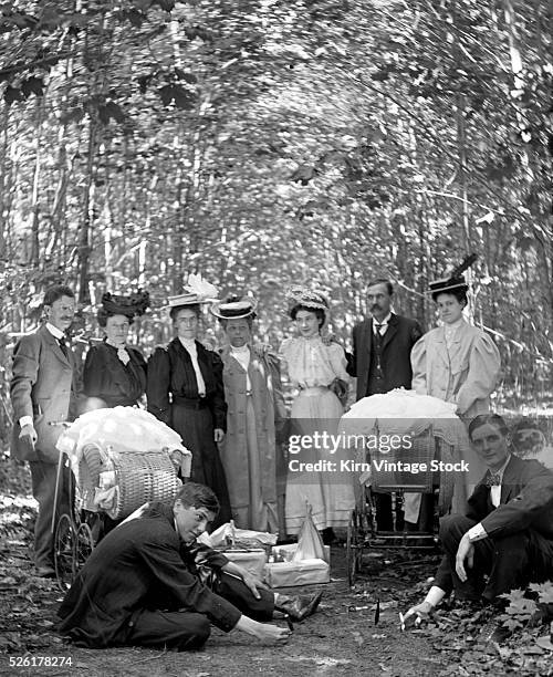 Group of adults with baby carriages pose in the woods, ca. 1905.