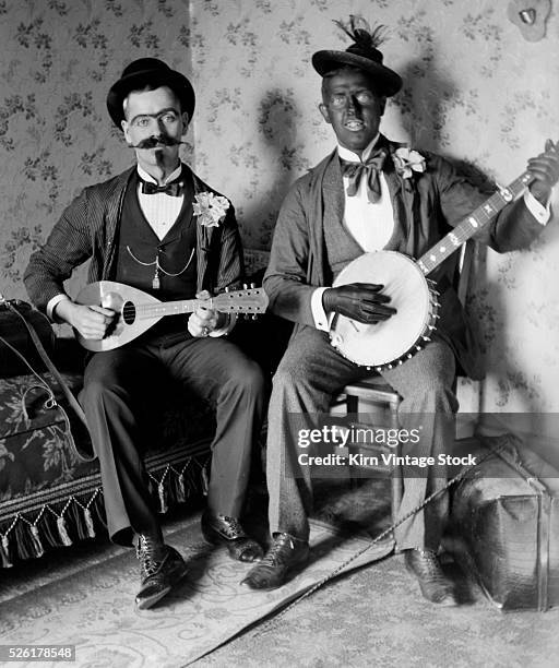 Two men, one in black face, play a mandolin and a banjo.