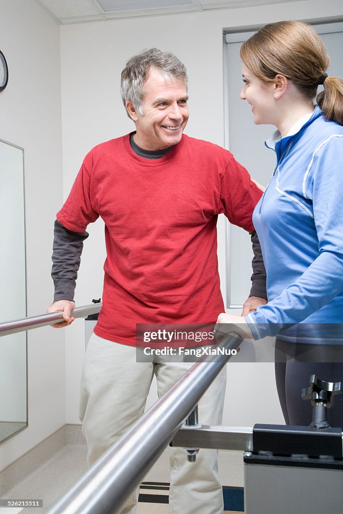 Woman helping man walk on crutches in hospital