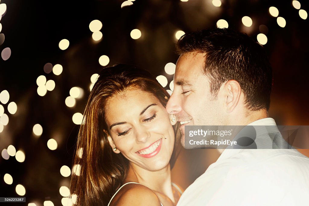 Good-looking couple embrace, smiling, under twinkling lights