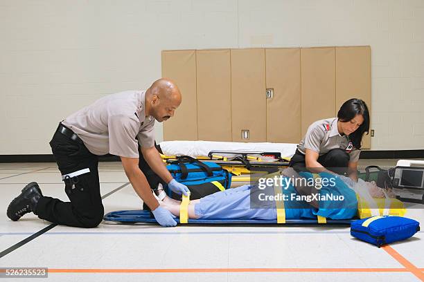paramedics strapping patient to stretcher in gymnasium - fallen heroes stock pictures, royalty-free photos & images