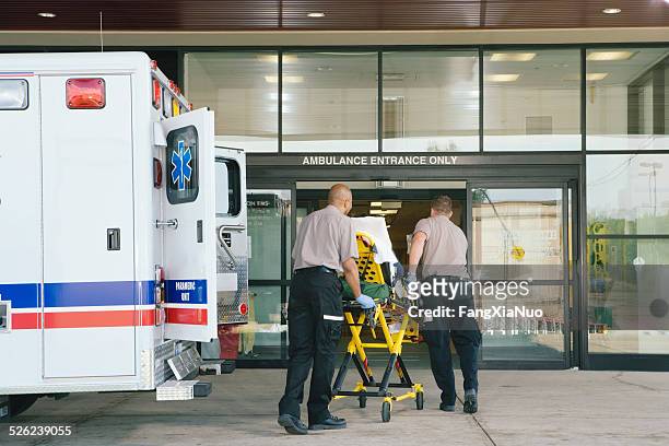 sanitäter mit patienten auf trage vom krankenwagen zur hospital - rettung stock-fotos und bilder
