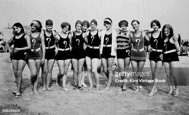 Group of flappers with question marks on their swim suits pose together on the beach.