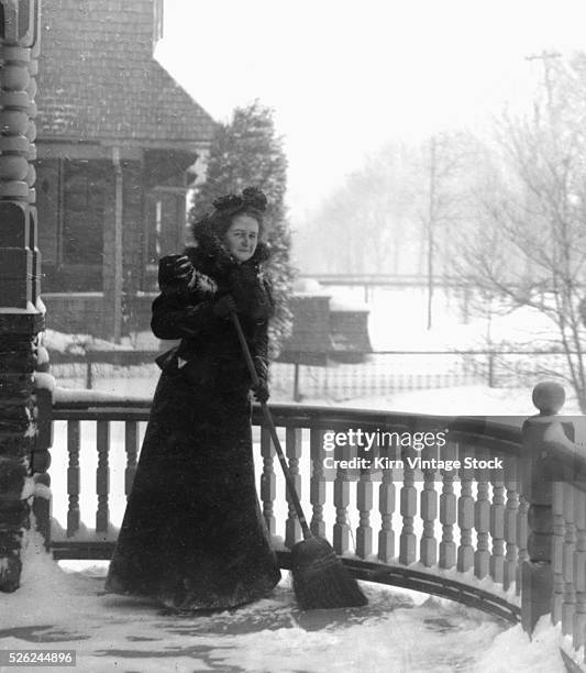 Victorian woman sweeps snow off her porch, ca. 1900