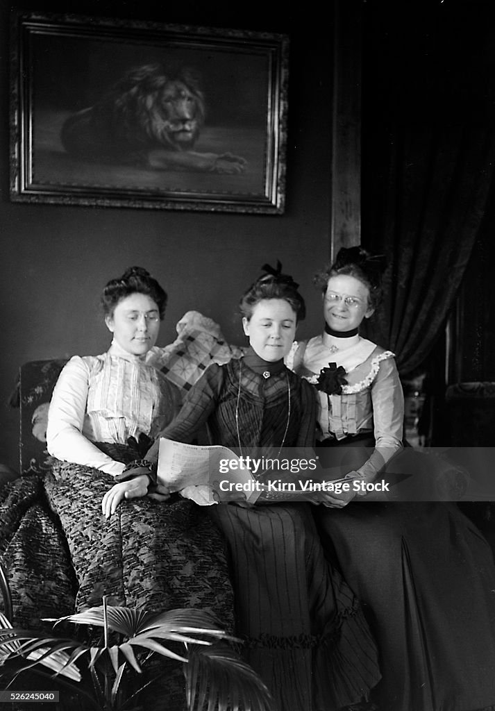 Three women look over some sheet music, ca. 1900