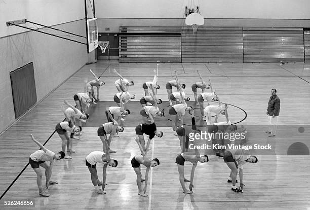 Teenage boys in class perform toe touches in unison.