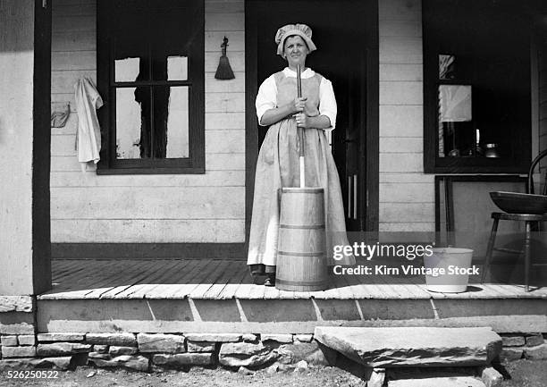 Woman churns butter on her porch, ca. 1910.