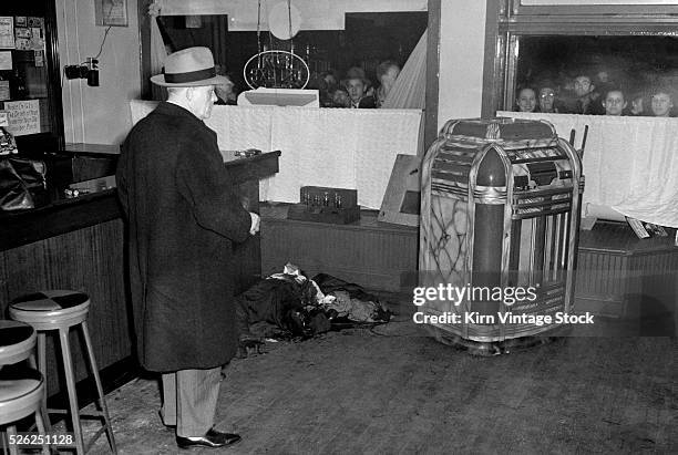 Chicago cop surveys a bar room murder scene while the public looks in through the front window.