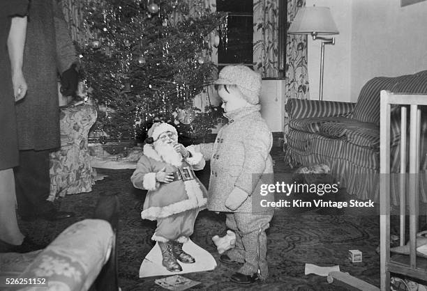 Young boy plays with cardboard Santa under the tree, ca. 1947.