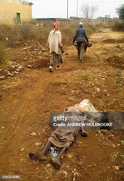 August 1992 - Men picking up bodies in a wheel barrow pass a dead woman lying on the ground, a victim of the famine that claimed more than 300,000...