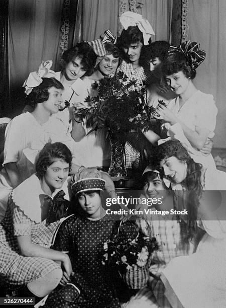 Young women gather together around a bouquet of flowers, c. 1910.