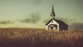 Old abandoned white wooden chapel on prairie at sunset.