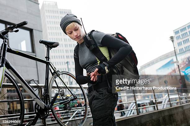 female bike messenger locking bike - bicycle messenger stock pictures, royalty-free photos & images