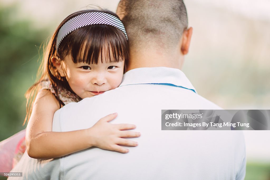 Toddler resting her chin on dad's shoulder in park