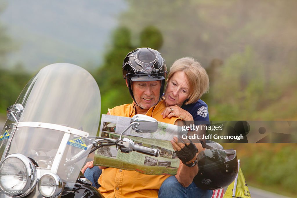 Older Caucasian couple reading map on motorcycle
