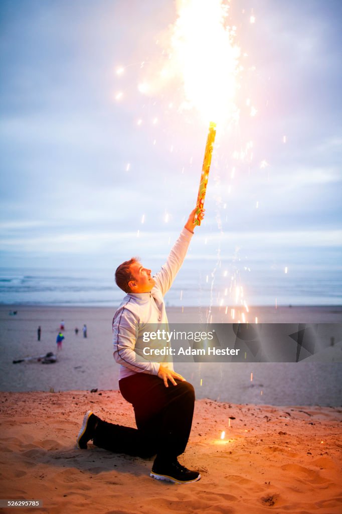 Caucasian man holding fireworks on beach