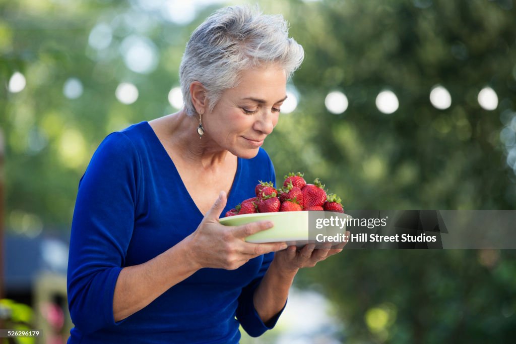 Caucasian woman smelling bowl of fresh strawberries