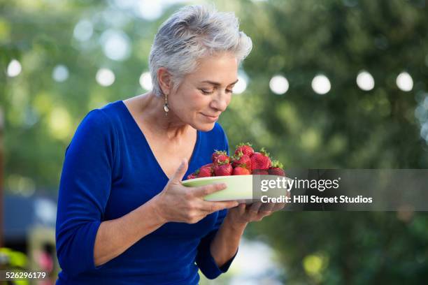 caucasian woman smelling bowl of fresh strawberries - ruiken stockfoto's en -beelden