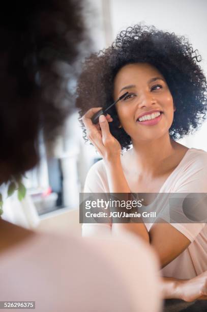 smiling woman applying mascara in mirror - applying mascara stock-fotos und bilder