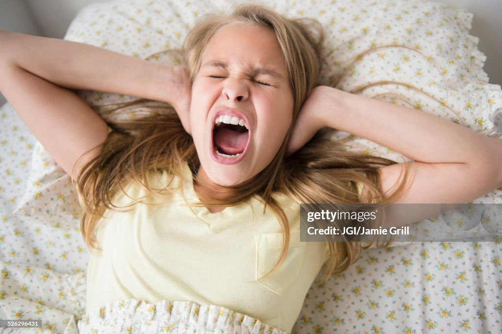 Shouting Caucasian girl covering her ears on bed