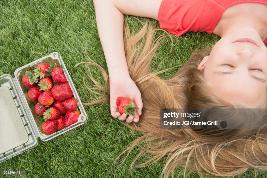 Caucasian girl holding strawberries on grassy lawn