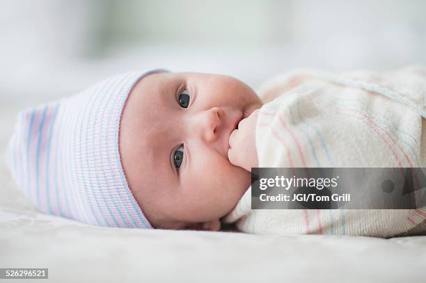 swaddled asian baby biting fingers on bed - manta de bebé imagens e fotografias de stock