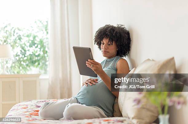 pregnant african american mother using digital tablet in bed - african american woman with tablet stockfoto's en -beelden