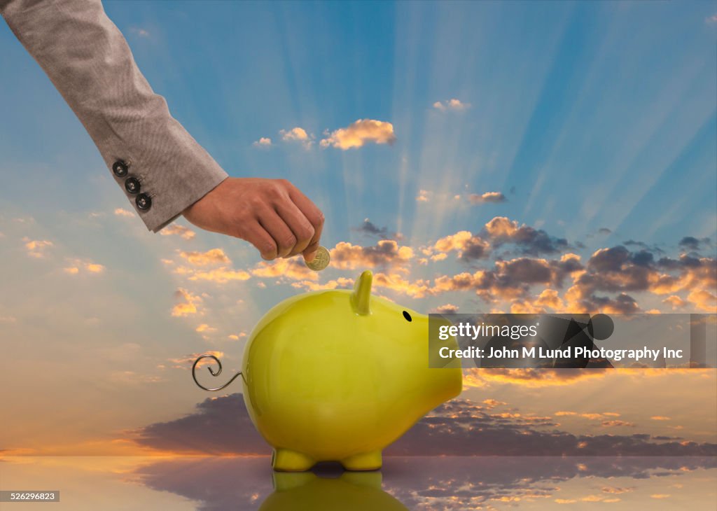 Mixed race businesswoman saving coin in piggy bank