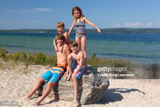 caucasian cousins standing on rock at beach - front view portrait of four children sitting on rock stock pictures, royalty-free photos & images