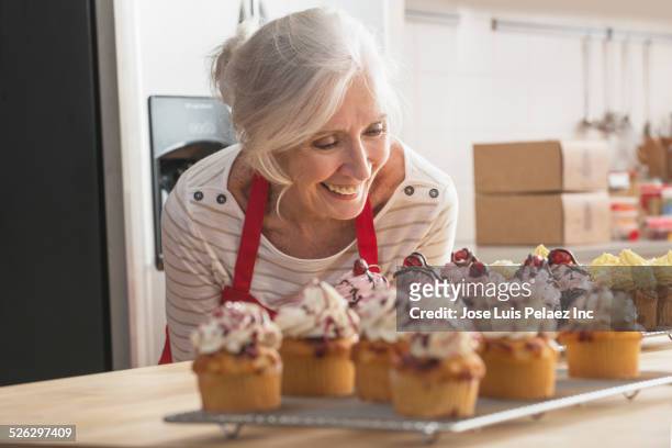 older caucasian woman with cupcakes in kitchen - woman baking stock-fotos und bilder
