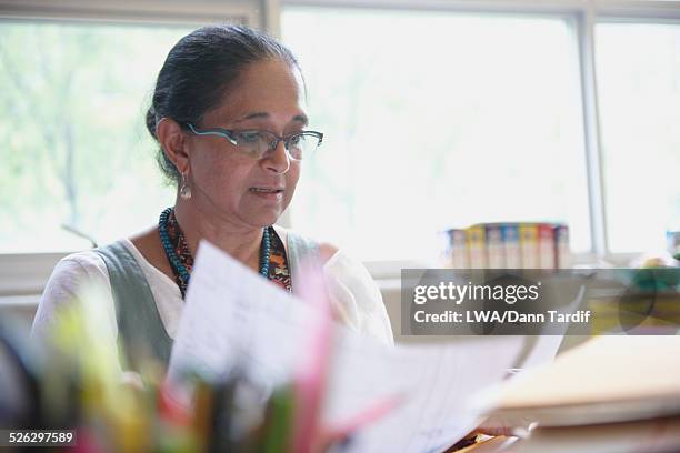 indian woman reading paperwork at desk - reading glasses imagens e fotografias de stock