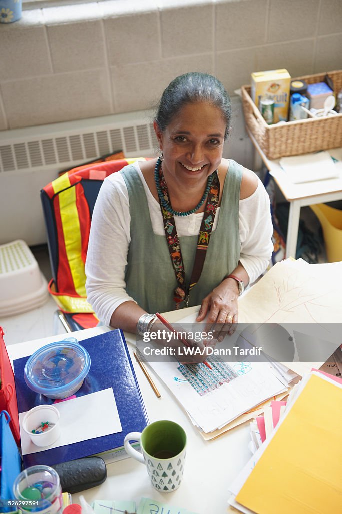 Indian teacher grading papers at desk in classroom