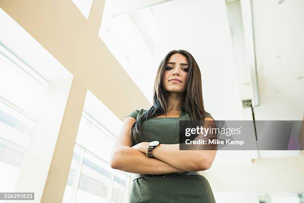 low angle view of hispanic businesswoman standing in office - braços cruzados mulher imagens e fotografias de stock