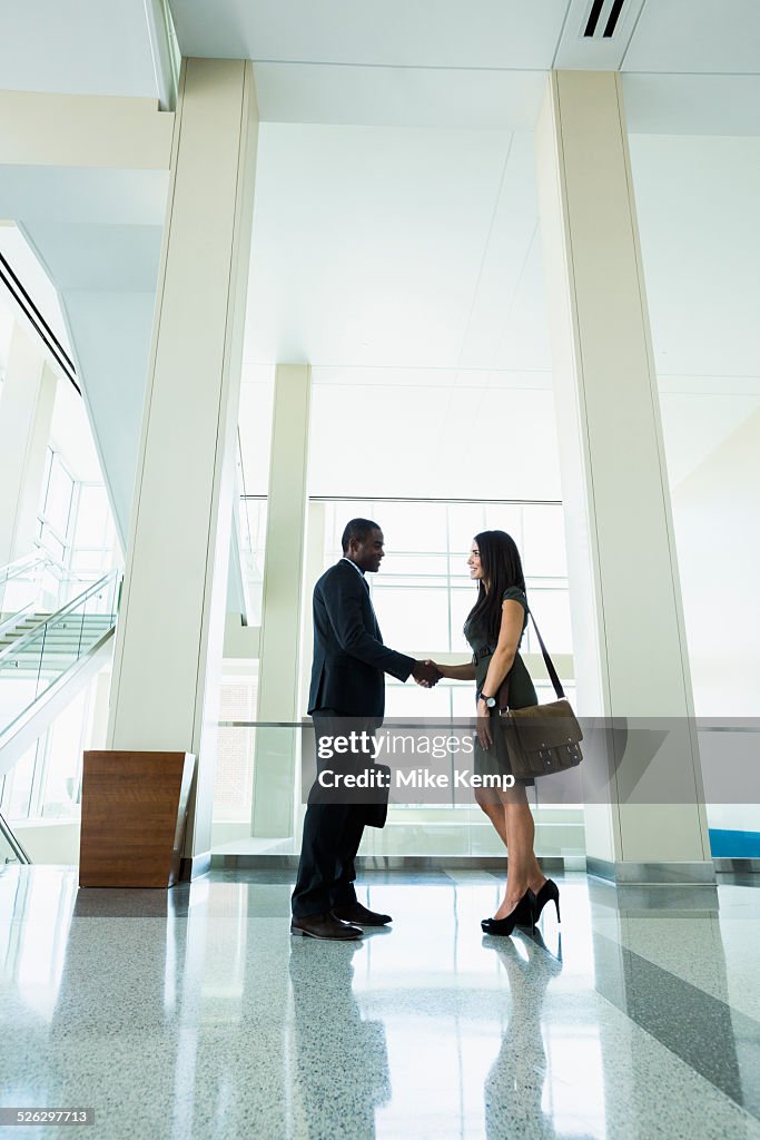 Business people shaking hands in office hallway